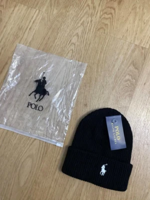 Svart ribbad mössa från Polo Ralph Lauren - Säljer en svart ribbad mössa från Polo Ralph Lauren med klassisk broderad logga i vitt framtill. Mössan har uppvikt kant och är perfekt för att hålla värmen under kyliga dagar. Stilren och enkel design som passar till det mesta.