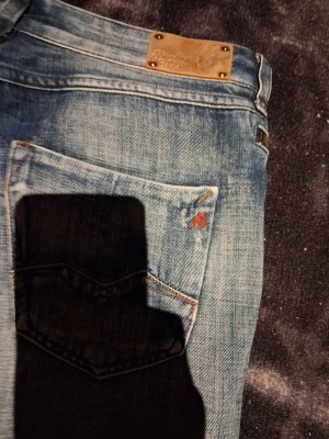 Replay blå jeans med tapered fit - Säljer ett par snygga blå jeans från Replay med klassisk femficksdesign och coola slitningar. Jeansen har en tapered passform som sitter skönt och ger en modern look. Metallmärke och broderad detalj på bakfickan. Perfekt för dig som gillar streetstyle.