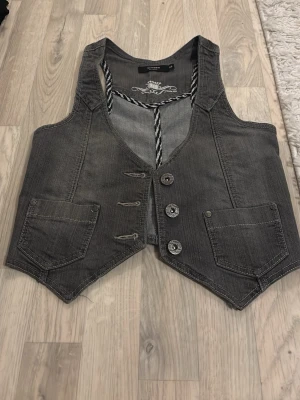 Grå jeansväst med knappar st 158 - Säljer en grå jeansväst från kappahl med snygga detaljer som tre metallknappar framtill och två fickor.  