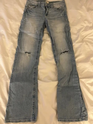 Ljusblå bootcut jeans från Gina Young - Snygga ljusblå jeans från Gina Young med bootcut-snitt och slitna detaljer vid knäna. Klassisk femficksmodell med knapp och dragkedja framtill. Jeansen har en cool tvättad look och är gjorda i mjukt bomullsmaterial.