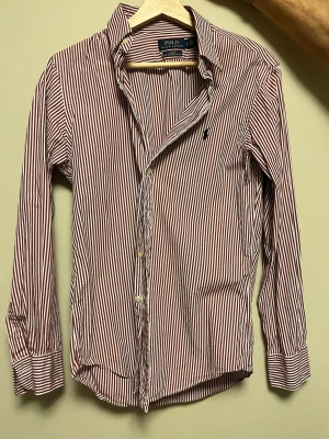 Polo Ralph Lauren skjorta  - Säljer en slim fit skjorta från Polo Ralph Lauren i rödvitt randigt mönster. Skjortan har långa ärmar, klassisk krage och knappar framtill. Tillverkad i stretchig bomull för extra komfort och snygg passform.