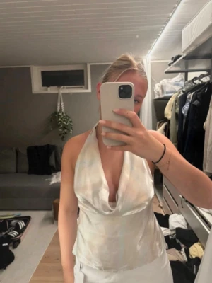 Silver/multifärgad halterneck - Säljer en superfin halterneck topp i glansigt satinliknande material. Toppen har djup urringning, öppen rygg och knyts med breda band i ryggen. Toppen är silverfärgad i grunden men skiftar i lite multifärg. Perfekt för dig som vill sticka ut med en elegant och trendig look. Finns en liten fläck (se sista bilden) som är där konstigt nog då jag endast testat den, det försvinner säkert i tvätten.