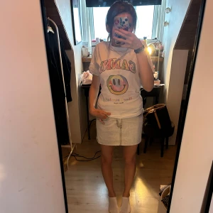 Ljusgrå jeanskjol med sömmar med fickor från gina  - Säljer en ljusblå jeanskjol i kort modell med klassiska fickor fram och bak, samt hällor för bälte. Kjolen har dragkedja och knapp framtill och är gjord i mjukt bomullsmaterial. Perfekt för dig som gillar en chill och enkel stil.