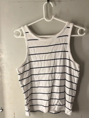 Randig vit linnetopp - Säljer 2  vita linnetoppar med tunna svarta horisontella ränder. Topparna är ärmlösa med breda axelband och har en ribbad kant vid halsen och ärmhålen. Perfekt för varma dagar och enkel att matcha med jeans eller shorts. Första är i stolek L och den andra i XL