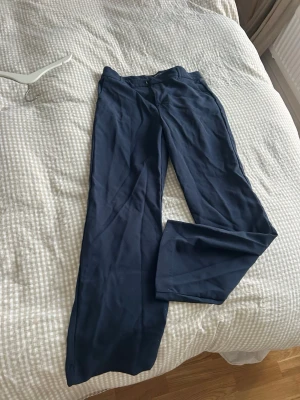 Marinblå wide byxor från Gina Tricot - Snygga marinblå byxor från Gina Tricot i storlek 38. De har ett wide snitt med raka, vida ben och klassisk midja. Materialet känns mjukt och lätt, perfekt för en chill och stilren look. Passar dig som gillar enkel och modern stil.