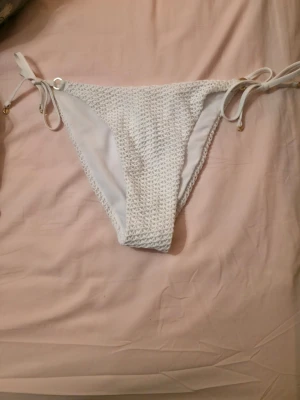 Nya bikini trosor 38  - Bilderna visar ett par vita virkade bikinitrosor med knytband i sidorna och små guldfärgade detaljer.