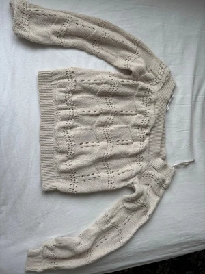 Beige stickad tröja med hålmönster - Säljer en beige stickad tröja med snyggt hålmönster och ribbade muddar vid ärmslut och nederkant. Tröjan har långärmade ärmar och en rund halsringning. Perfekt för dig som gillar en chill och mysig stil. Kan även användas som off shoulder. 