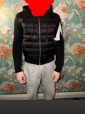 Svart dunväst från Moncler - Säljer en svart cardigan från Moncler med quiltad design och dragkedja framtill. Den har en stilren look och passar perfekt året om. Klassisk Moncler-logga på sidan och praktiska fickor med dragkedja.
