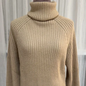 Beige ribbad polotröja stickad - Säljer en beige ribbad polotröja med hög krage och lång ärm. Tröjan är stickad i ett mjukt material pch breda armar. Använt endast 1 gång! 