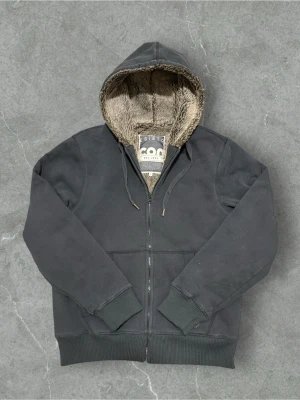 Fodrad vintage zip hoodie  - Mysig svart hoodie från Conbipel med dragkedja och huva. Insidan är fodrad med mjuk fuskpäls i beige/brun ton, perfekt för kyliga dagar. Klassisk passform med ribbade muddar och snörning i huvan. Snygg och varm till höst och vinter!