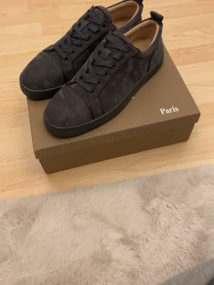 Christian Louboutin gråa mockasneakers - Säljer ett par gråa sneakers från Christian Louboutin i mjuk mocka med klassisk röd sula. Skorna har rund tå, platt sula och snörning. Insidan är beige och märkt med Louboutin Paris. Kommer med originalkartong, dustbag och äkthetskort.