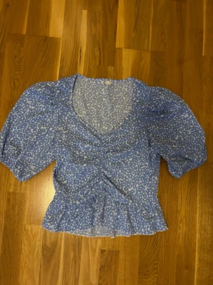 Blommig blå blus med puffärm - Söt blommig blus i blått och vitt från Cubus, storlek M. Modellen har v-ringning, puffiga trekvartsärmar och volangkant nedtill. Tunn och luftig med rynkdetaljer framtill, perfekt för vår och sommar.