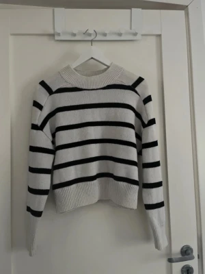 Randig stickad tröja från Amisu - Säljer en vit och svart randig stickad tröja från Amisu i storlek S. Tröjan har en rund halsringning med bred ribbad kant, långa ärmar och en loose passform. Materialet är mjukt och stickat, perfekt för kyliga dagar. Ganska nopprig och lite mörkare vit 