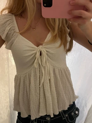 Vit omlottopp med knyt från 157 - Supersöt vit topp från 157 i storlek XS. Modellen har v-ringning, volangärmar och knyt framtill som ger en omlottkänsla. 💞