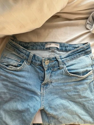 Ljusblå low waist jeans från Bershka - Säljer ett par ljusblå jeans från Bershka med low waist-passform. Jeansen har klassisk femficksdesign, raka ben och är tillverkade i mjukt denimtyg. Perfekta för dig som gillar en avslappnad och tidlös look.