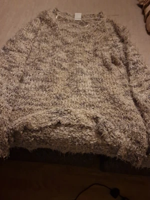 Beige stickad tröja från Vero Moda - Mysig stickad tröja från Vero Moda i beige och grå toner. Tröjan har en fluffig struktur och lång ärm, perfekt för kyliga dagar. Passformen är normal och materialet känns riktigt mjukt och skönt. Priset som står gäller, kan möjligtvis diskuteras🫶