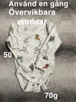 Vit omlottbody med drakmönster - Säljer en vit omlottbody med gulligt mönster av drakar och små kaniner. Bodyn har övervikbara muddar och tryckknappar i grenen för enkel påklädning. Perfekt för de allra minsta. 🌸 Använd en gång. Övervikbara muddar. Storlek 50