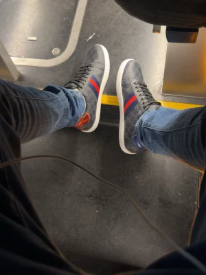 Gucci ace skor - Säljer ett par snygga Gucci sneakers i mörkgrått med klassiskt monogrammönster och röd-blå rand på sidan. Skorna har svarta snören, vit platt sula och detaljer i rött och blått på hälen. Kommer med originalkartong och dustbag. Pris kan diskuteras och bra skick