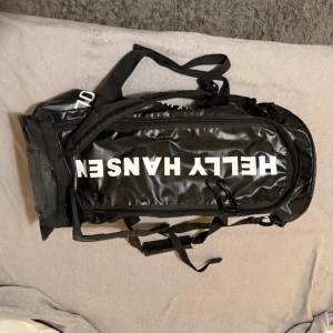 Svart Helly Hansen ryggsäck Renault - Säljer en svart ryggsäck från Helly Hansen med Renault-tryck. Väskan har flera fack med dragkedja, robusta handtag och justerbara axelremmar. Materialet är slitstark syntet med blank finish och tydliga vita logotyper. Perfekt för dig som vill ha en cool och praktisk väskan.  Pris kan diskuteras vid snabb affär 