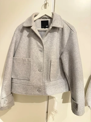 Grå overshirt från 157 med stora fickor - Snygg grå overshirt från 157 med klassisk krage, stora framfickor och knappar både framtill och vid ärmslut. Jackan har en boxig och lite croppad passform som ger en chill vibe. Perfekt att slänga över en hoodie eller t-shirt när det är lite kyligt ute.