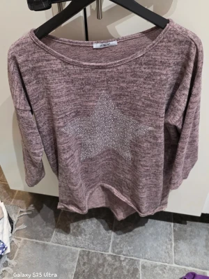 Ljuslila tröja med stjärndetalj L  - Säljer en mjuk och skön ljuslila tröjai storlek L. Tröjan har lång ärm och ett stort glittrigt stjärnmotiv framtill. Materialet är en blandning av polyester, viskos och elastan vilket gör den stretchig och bekväm. Perfekt för dig som gillar lite extra bling.