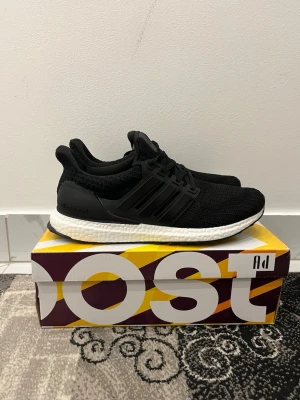 Adidas Ultraboost svartvita sneakers - Svarta Adidas Ultraboost sneakers med stickad ovandel och klassiska tre ränder på sidan. Skorna har en vit, responsiv Boost-sula och snörning framtill. Perfekta för dig som gillar stilrena och bekväma sneakers med modern design.