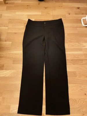 Svarta kostymbyxor med raka ben - Säljer ett par klassiska svarta kostymbyxor med raka ben och två knappar i midjan. Byxorna har en enkel och stilren look, perfekta till en snygg outfit. Materialet känns mjukt och har en lätt stretch för extra komfort. Lågmidjade. Priset går att diskutera. 