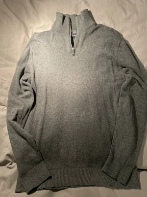 Grå half zip tröja från Jack & Jones - Snygg grå långärmad tröja från Jack & Jones med half zip och hög krage. Tröjan har ribbade muddar vid ärmslut och nederkant, vilket ger en schysst passform. Perfekt för dig som gillar stilrena och enkla plagg. Materialet känns mjukt och är troligtvis bomull eller syntet. Nyskick!