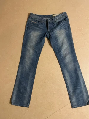Blå Diesel jeans - Säljer ett par blå jeans från Diesel i storlek W28 L32 med klassisk femficksdesign och raka ben. Jeansen har en snygg tvätt med ljusare partier framtill och bak. Perfekt för dig som gillar stilrena och tidlösa jeans. 