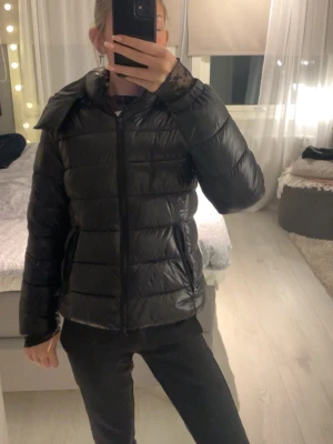 Svart pufferjacka med huva - Säljer en svart pufferjacka från Lager 157. ( Ena sidan man stänger huvan till är en knapp av! ) Säljer för lågt pris, då jag bara vill bli av med den!