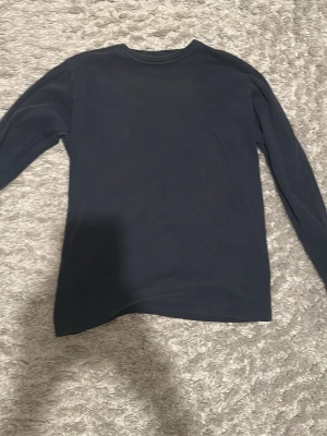 Mörkblå långärmad topp från Emilio - En enkel och stilren mörkblå långärmad topp från Emilio. Tillverkad i mjuk bomull med rund halsringning och rak passform. Perfekt att matcha med jeans eller kjol för en clean look.