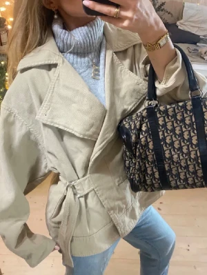 Beige oversize kappa från Dagmar - Säljer en beige jacka med bred krage och bälte i midjan. Jackan har en loose och oversized passform, stora fickor och är tillverkad i ett mjukt bomullsmaterial. 