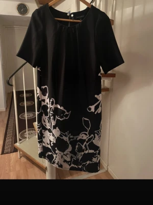 Bernd Berger Black Dress with White Floral Print – Size 38 - Elegant black dress from Bernd Berger in size EU 38. Minimalist design with short sleeves and a beautiful white floral print at the hem, giving it a timeless and classy look. Features a zip closure at the back and a flattering, straight fit. Perfect for work, dinner, parties or more formal occasions. Easy to dress up with heels or keep simple with flats. Condition: Very good condition, no visible flaws. Color: Black with white floral pattern Size: EU 38 (please check measurements if needed) Feel