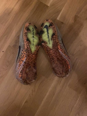 Nike mercurial vapor 16 - Säljer ett par Nike fotbollsskor i grått och orange med svart leopardmönster och stora svarta swoosh-loggor. Skorna har en strumpliknande passform och är tillverkade i syntetmaterial för bästa grepp på planen. Perfekta för dig som vill sticka ut på matchen!