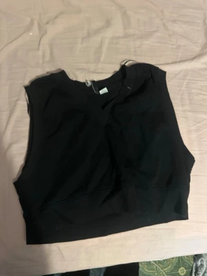 Svart croppad linnetopp/väst - Säljer en svart croppad linnetopp/väst med v-ringning. Toppen är ärmlös och har en enkel, stilren design som passar perfekt till jeans eller kjol. Materialet känns mjukt och stretchigt, vilket gör den bekväm att bära hela dagen.