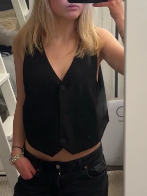 Väst från MNG - Snygg svart väst från MNG med v-ringad hals och två stora knappar framtill. Perfekt att styla över en t-shirt eller skjorta. Använd få gånger!🙌☺️Oversize passform på mig som brukar ha XS-S i storlek! 