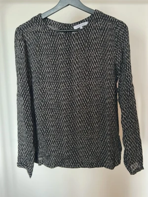 Neo Noir Blus, S - Neo Noir Blus i storlek S. Axelbredd 39, längd 62. Bak på ryggen så finns en stängning med knappar.