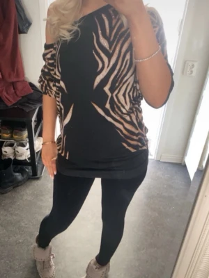 Zebramönstrad topp från Gizia - Säljer en svart topp från Gizia med zebramönster i beige och bruna toner. Toppen har en lös passform, korta ärmar och är dekorerad med små guldfärgade nitar för extra bling. Materialet känns mjukt och stretchigt, perfekt för dig som gillar statementplagg.