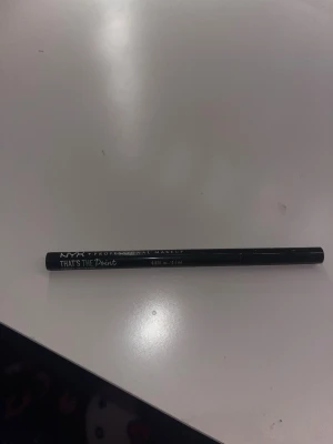 NYX That's The Point Eyeliner - Säljer en svart flytande eyeliner från NYX, That's The Point. Pennan har en spetsig filtspets som gör det enkelt att skapa både tunna och dramatiska linjer. Perfekt för skarpa vingar och detaljerad ögonmakeup. Förpackningen är svart och stilren.