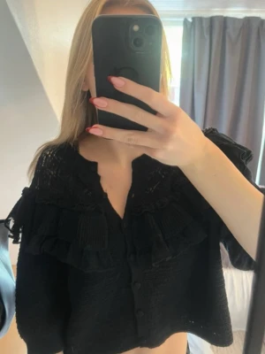 Svart kofta med volang - Säljer en svart stickad kofta ifrån Zara med fina volangdetaljer och knappar framtill. Storleken är L men den sitter exakt som en S. Supersöt! 💘