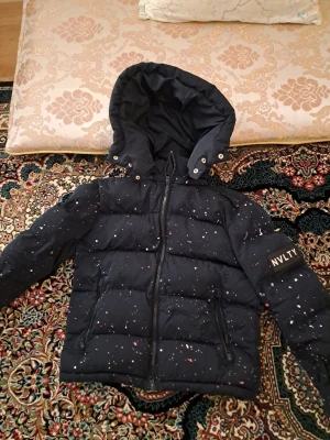 Mörkblå pufferjacka från NVLTY S - Säljer en mörkblå pufferjacka från NVLTY i storlek S. Jackan har avtagbar huva, dragkedja framtill och coolt stänkmönster i vitt och rosa. Perfekt för kalla dagar och riktigt snygg streetstil. Två fickor med dragkedja på sidorna och patch med logga på ärmen. Lägg gärna prisförslag!