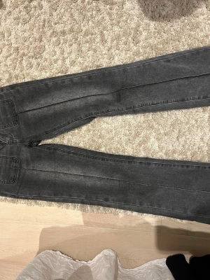 Gråa bootcut jeans med fickdetaljer - Säljer ett par gråa bootcut jeans med snygga framfickor och dubbla knappar i midjan. Jeansen har låg midja och markerade sömmar längs benen för en cool look. Bakfickorna har lock och knapp. Perfekta till en enkel topp eller hoodie.
