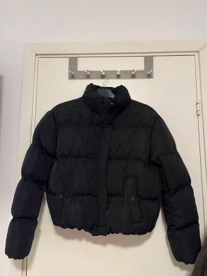 Svart pufferjacka från FB Sister - Säljer en svart pufferjacka i storlek M. Jackan har hög krage, dragkedja och tryckknappar framtill samt två fickor med knappstängning. Den är quiltad och har en lite croppad passform som ger en trendig look. Jackan är använd 1 gång. Pris kan alltid diskuteras!🤗