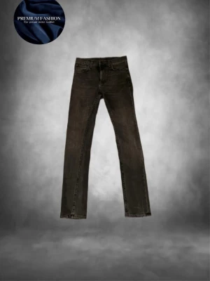 Nudie jeans grå/svart - Tja säljer nu ett par feta grå/Svarta jeans från Nudie  med slim passform och klassisk femficksdesign. Jeansen har svarta sömmar, knapp och dragkedja framtill  Perfekt för dig som gillar en clean och stilren look. Skicket är helt perfekt som nytt ungefär och storleken är w28 l32 passar dig som är runt 170-183cm lång skulle jag tro!! Har du några övriga frågor är de bara att höra av sig🙌🏼mvh em_resell🤩