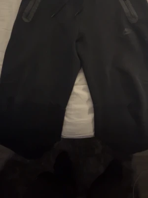 Svarta Nike tech mjukisbyxor - Säljer ett par svarta mjukisbyxor från Nike i storlek S. Byxorna har dragsko i midjan och dragkedjor på fickorna. Sköna och stilrena med en loose fit. Bra skick, pris kan diskuteras!
