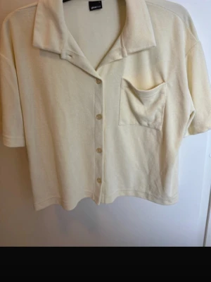 Beige kortärmad skjorta Gina Tricot - Kortärmad skjorta i beige från Gina Tricot. Skjortan har klassisk krage, knappar framtill och en bröstficka. Tillverkad i mjukt frottématerial som ger en chill vibe och avslappnad look.