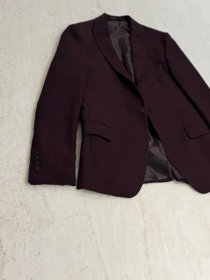 Mörklila kavaj   - Slim fit kavaj i mörklila från Daniel Alves. Kavajen har klassisk krage, en knapp framtill och fickor med lock. Insidan är fodrad med paisleymönstrat tyg i lila toner. Materialet är 65% polyester och 35% viskos. Perfekt för dig som vill ha en stilren och modern look.