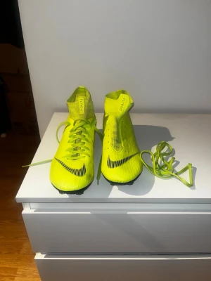 Nike Mercurial Superfly Flyknit (2016-2017) - Nike Mercurial Superfly V AG/FG (MG: Multi Ground) Flyknit (2016-2017) – Neon Gul/Svart Mercurial Superfly V Flyknit-skor! Släppta 2016-2017, dessa skor är designade för fart, precision och komfort på fasta underlag. Den neon gula och svarta designen gör att de sticker ut på planen, medan Flyknit-ovandeln och Dynamic Fit-kragen säkerställer en tajt, strumpliknande passform. Skick: Slitna, men i gott skick – väl underhållna och fullt funktionella Storlek: 45 Funktioner: • Flyknit-ovandel för anpa
