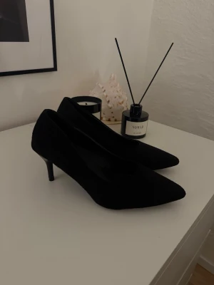 Svarta pumps med spetsig tå - Säljer ett par klassiska svarta pumps med spetsig tå och låg klack. Skorna är i mocka och har en elegant siluett som passar perfekt till jeans eller klänning. Supersnygga och tidlösa, perfekta för dig som gillar stilrena detaljer.