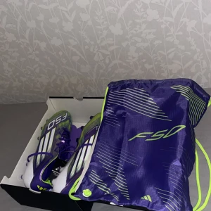 Adidas F50 lila fotbollsskor - Säljer ett par Adidas F50 fotbollsskor i lila, vitt och neongrönt. Skorna har snörning och klassisk Adidas-design med tre vita ränder på sidan. Medföljer en matchande F50-påse. Perfekta för dig som vill sticka ut på planen!